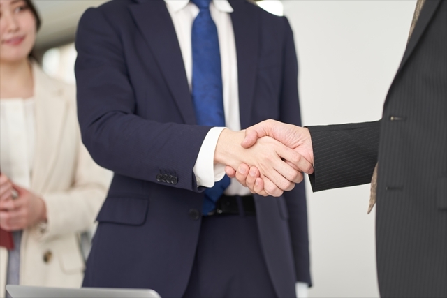 2023年4月版の設定では、スーツを着た2人が給与交渉を行っており、握手している一方、近くに立っている第三者が部分的に見えている。.