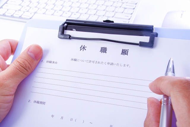 ペンを持ち、クリップボードに添付された日本語の休暇申請書に正確に記入している人。背景にはキーボードがある。この細心の注意を要する作業は、転職の際の重要なポイントとなる可能性がある。.